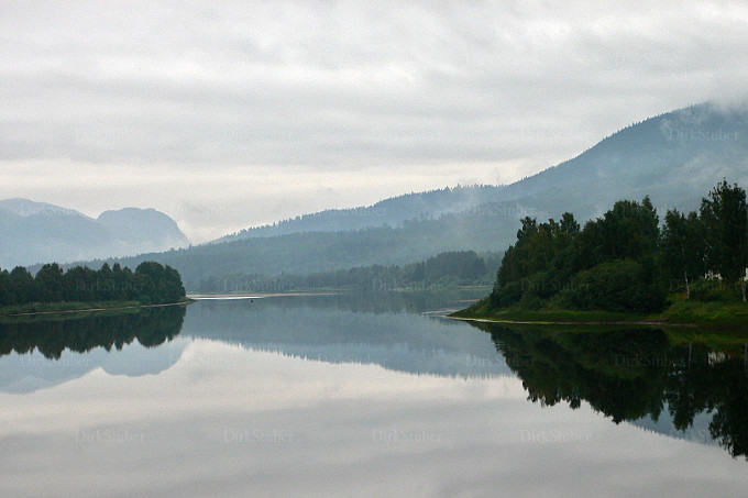 Ein See mit dem Spiegelbild der vernebelten Berge im Hintergrund